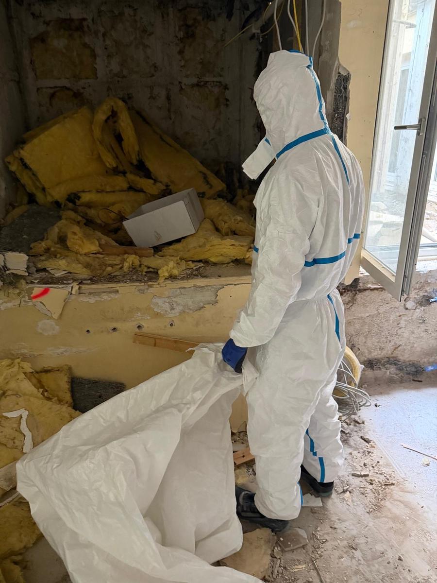 Mitarbeiter in Schutzausrüstung entfernt alte Dämmwolle